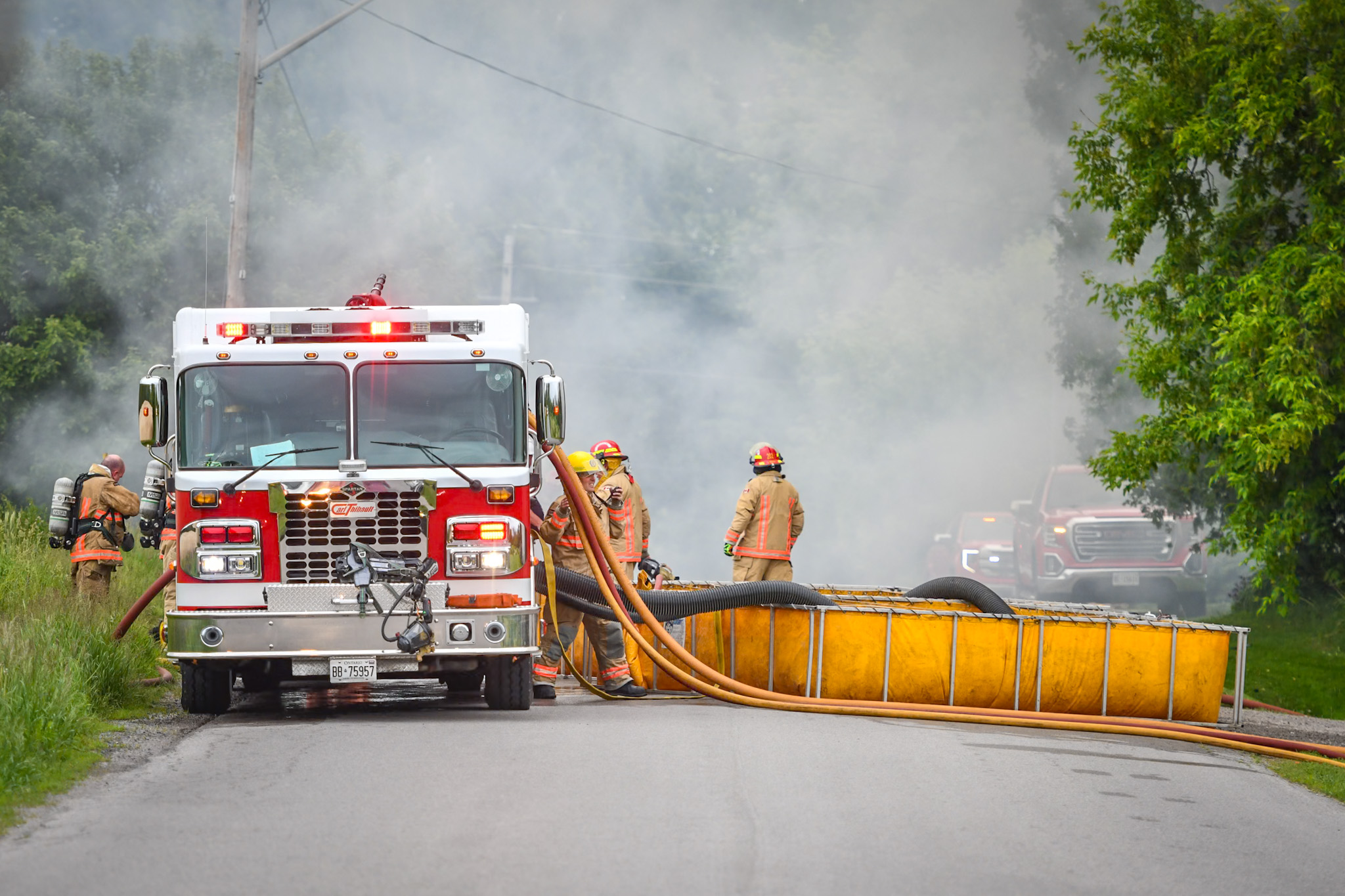 Firefighters stanring next to a fire truck fighting a road side fire.